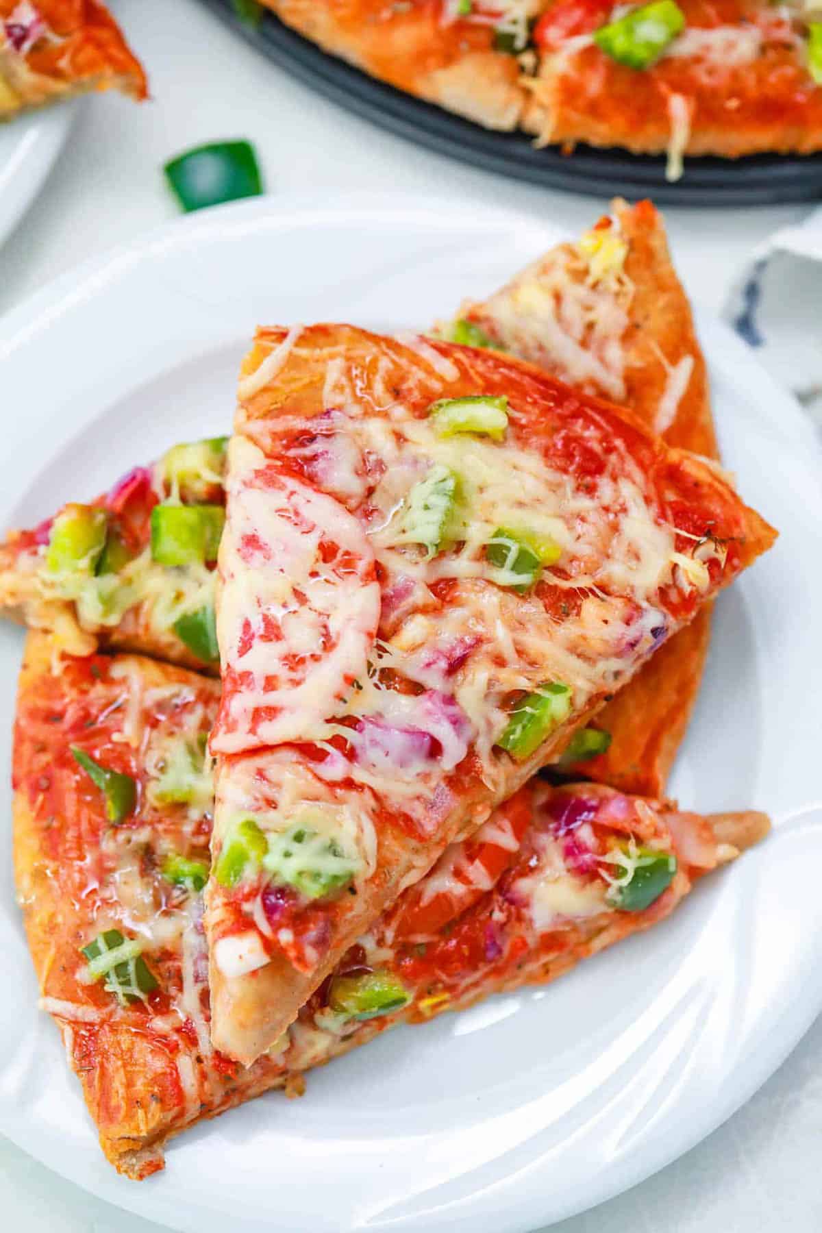 Overhead shot of a stack of veggie pizza on a white plate.