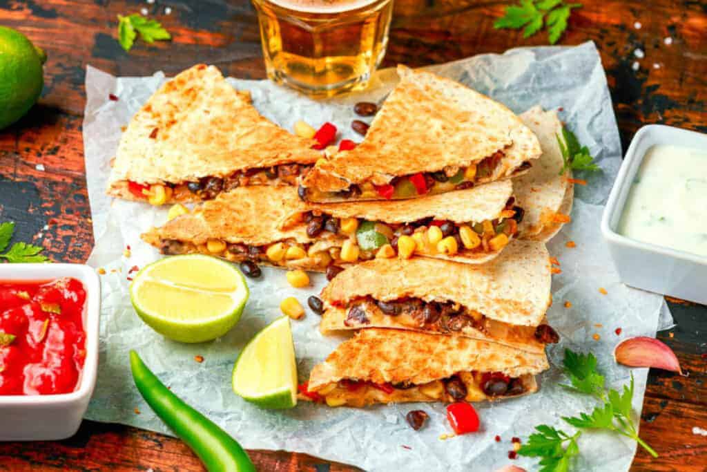 Veggie quesadillas stacked on parchment paper with herbs, lime, and ،.