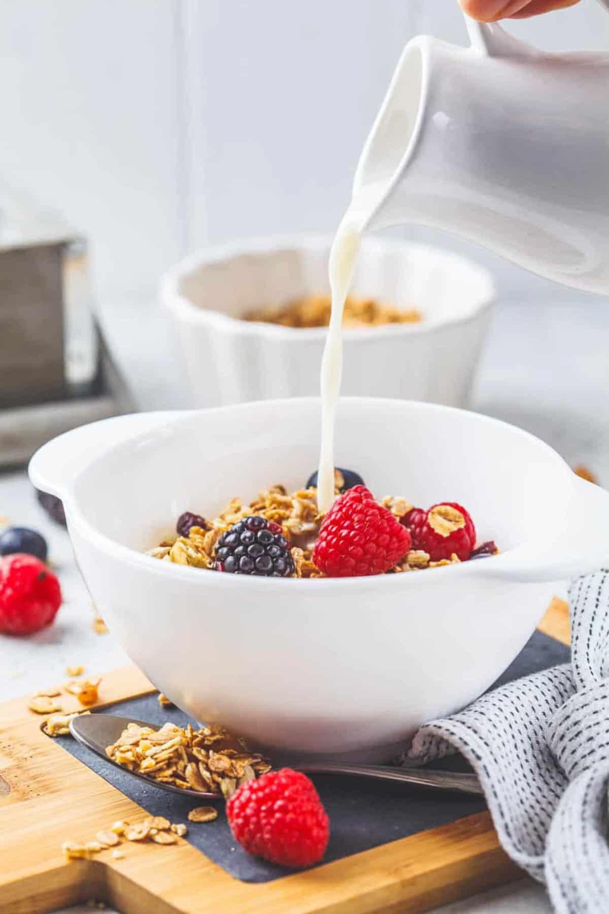 Pouring milk into a white bowl of granola with berries.