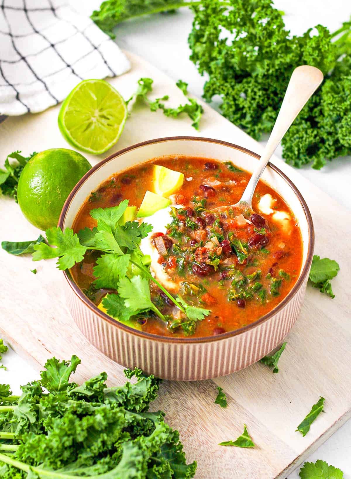 Kale and black bean soup, served in a grey bowl, garnished with avocado, cilantro, and sour cream.