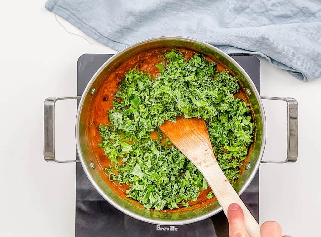 Kale added to black bean soup in a large pot on the stove.