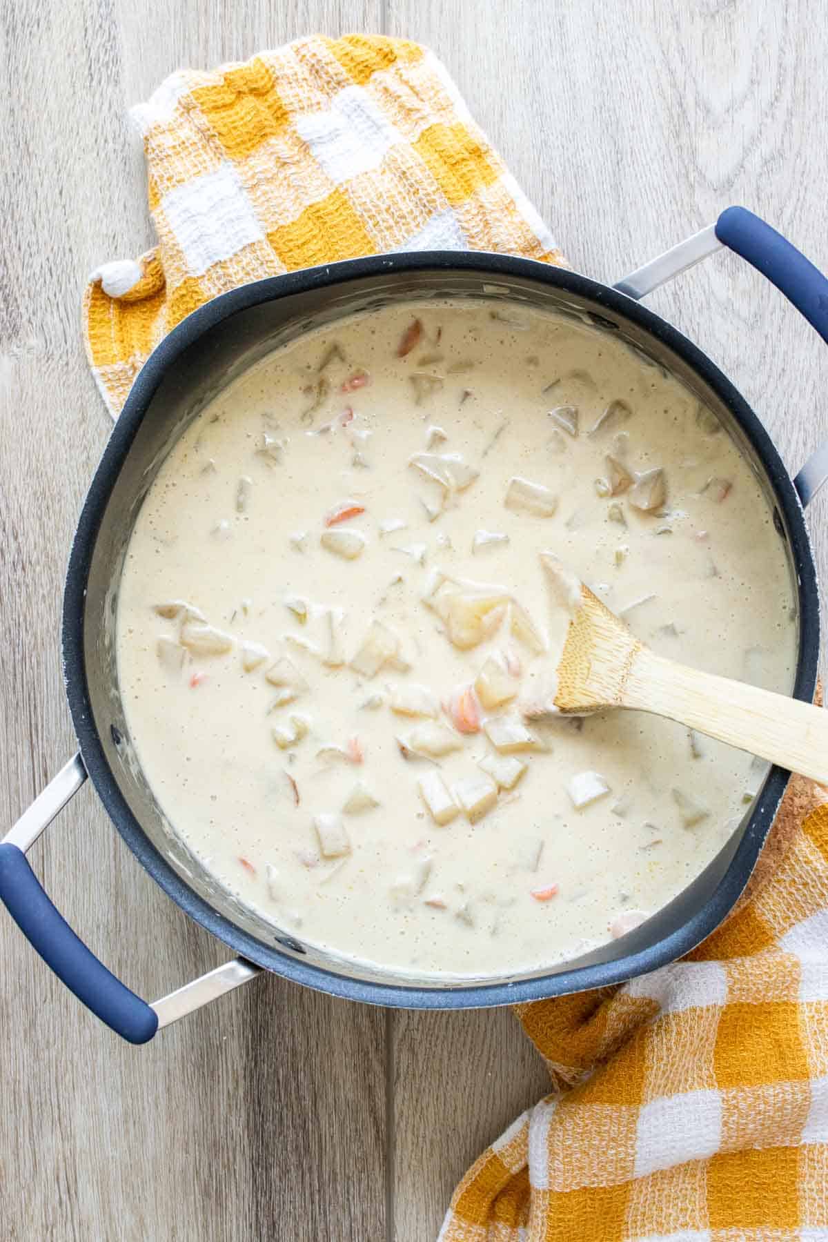 Wooden spoon mixing a creamy vegetable soup in a black pot.