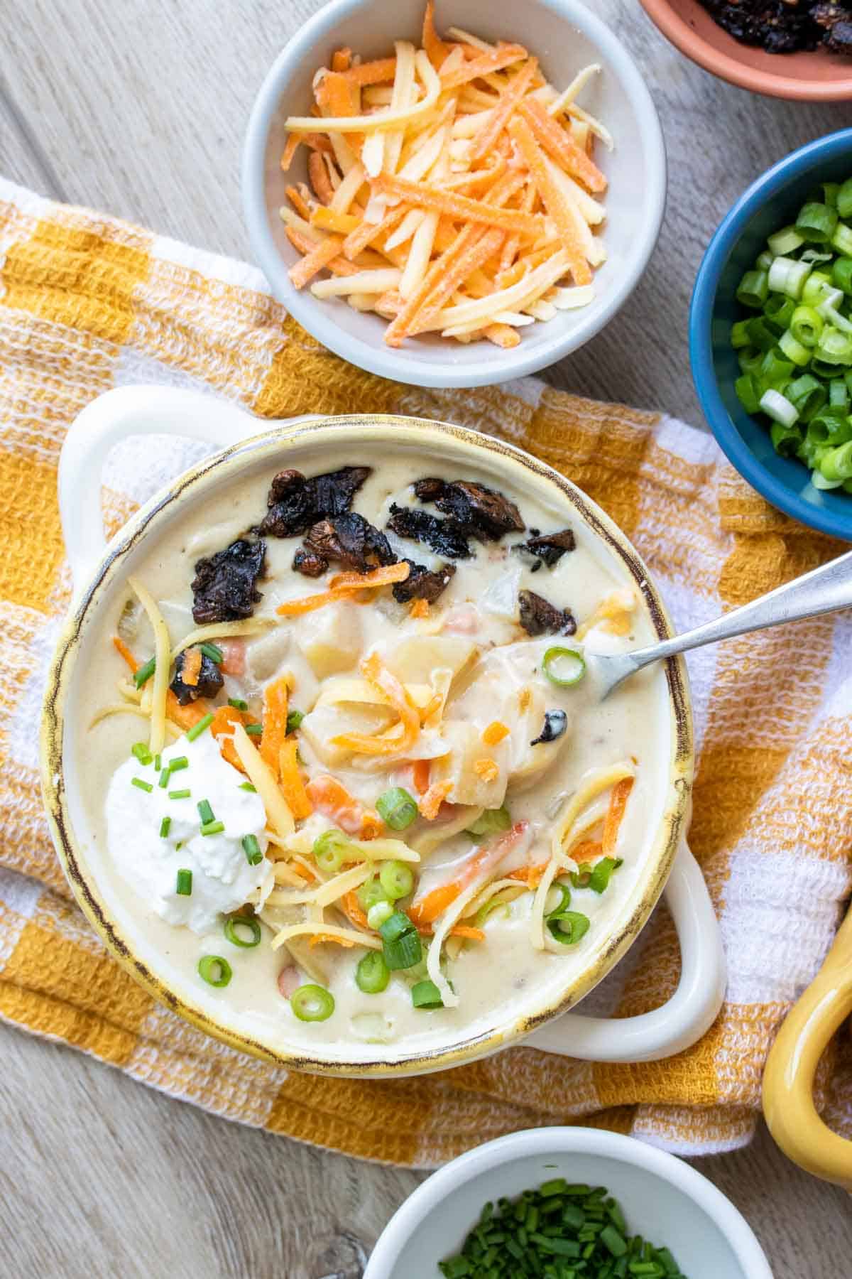 Spoon getting a bite from a cream bowl with potato soup covered in toppings.