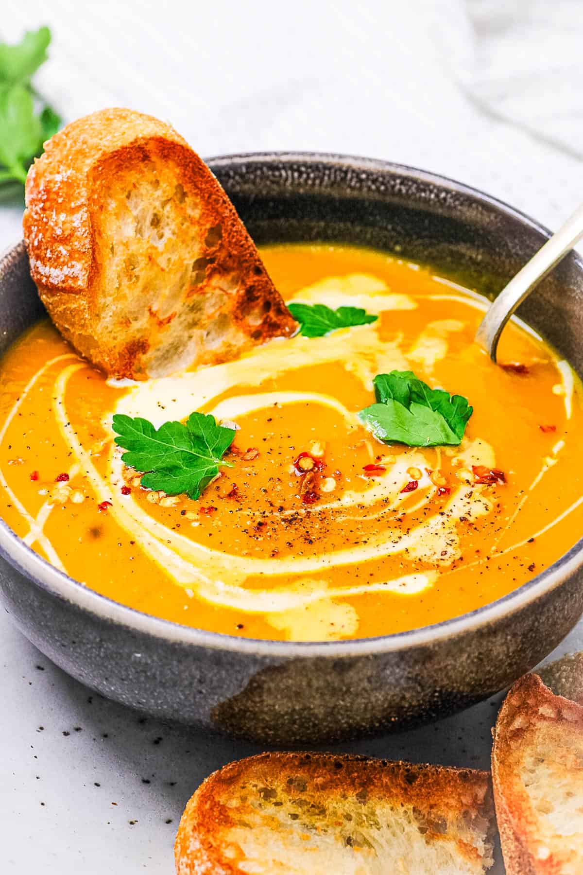 Curried sweet potato soup served in a black bowl, topped with coconut cream, crostini, and cilantro.