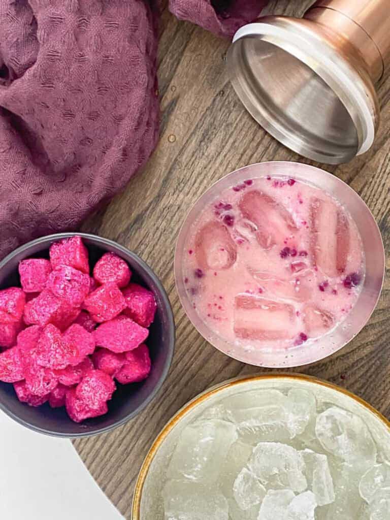 An overhead shot of a shaker full of the dragon drink next to a towel and small cup of cubed dragon fruit.