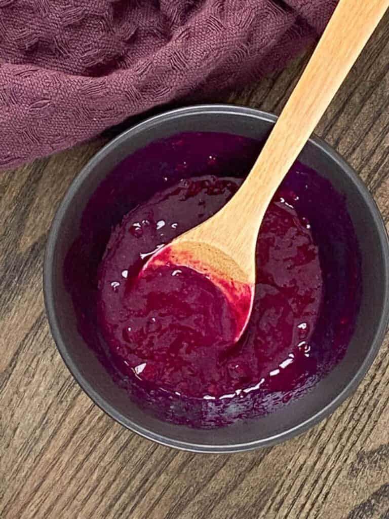 An overhead shot of a small dish of dragon fruit paste with a small wooden spoon.