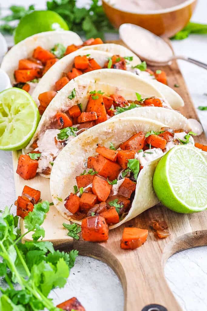 Easy sweet potato tacos with black beans and a spicy yogurt sauce served on a wooden cutting board.
