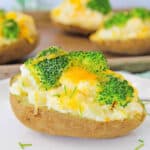 Healthy baked potato topped with broccoli and cheese, served on a white plate.