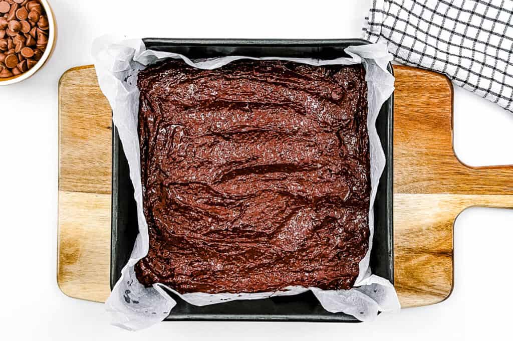 Flourless brownie batter added to a baking dish lined with parchment paper.