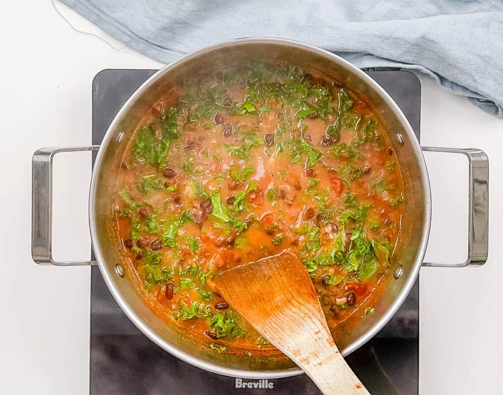 Healthy black bean and kale soup simmering in a pot on the stove.