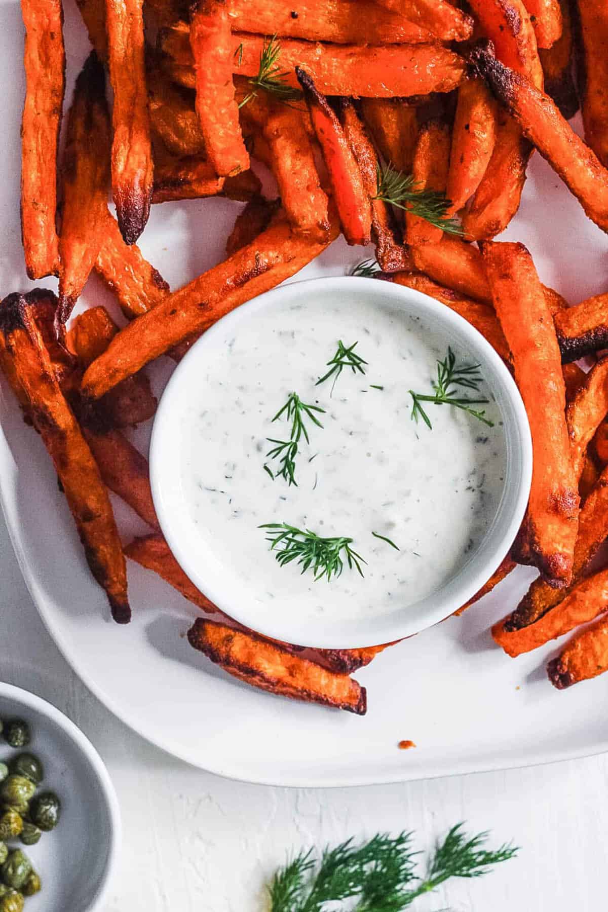 Homemade vegan tartar sauce served in a white bowl, with sweet potato fries on the side.