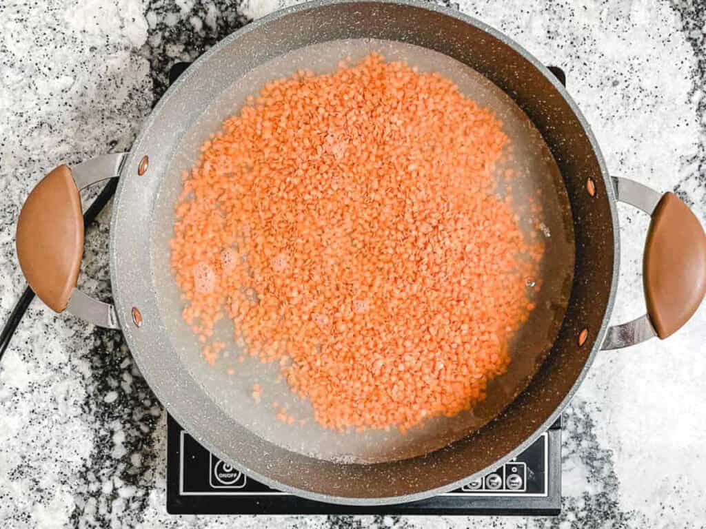An overhead shot of a pot of red lentils with water.