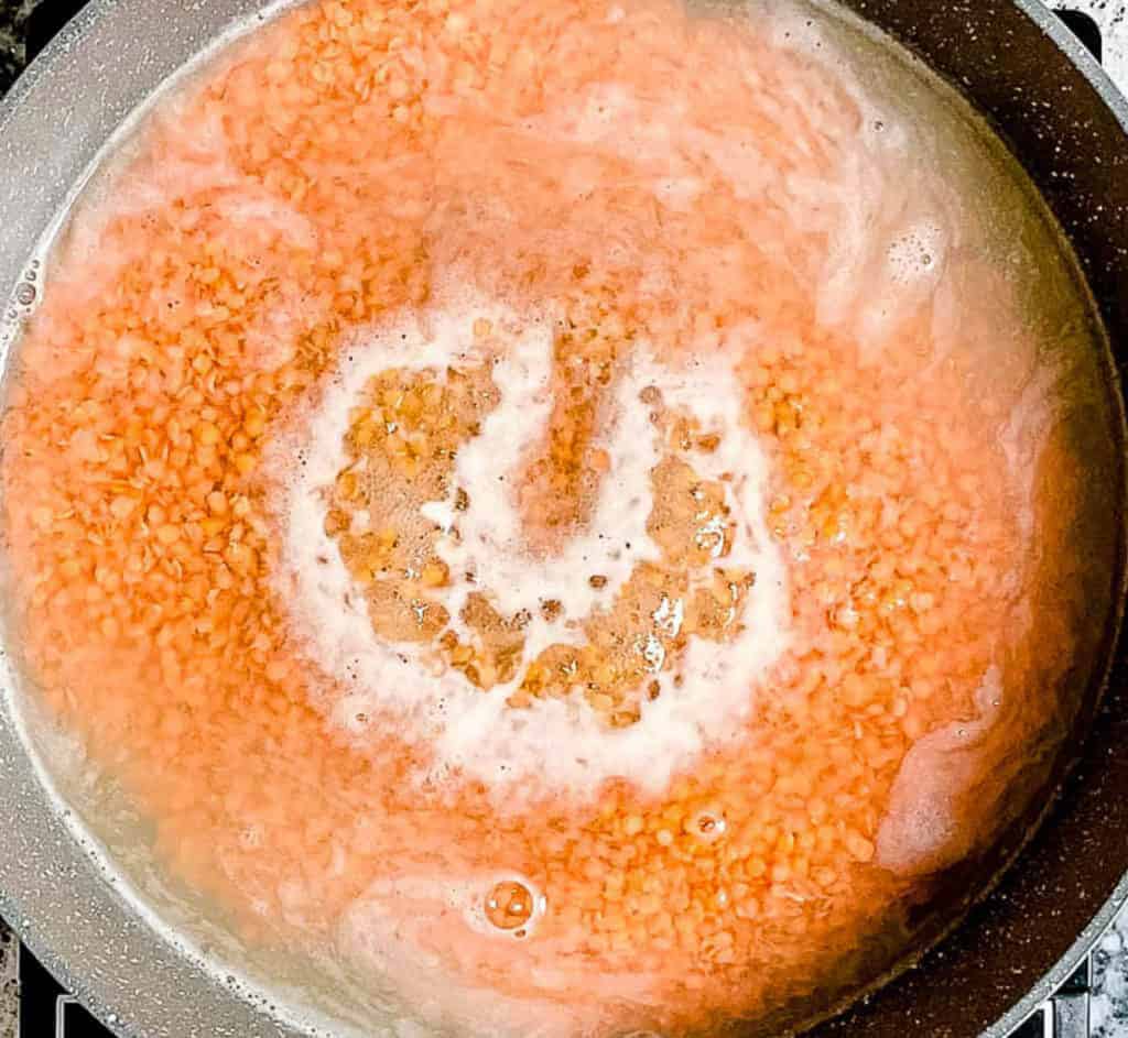An overhead shot of red lentils in water in a pot.