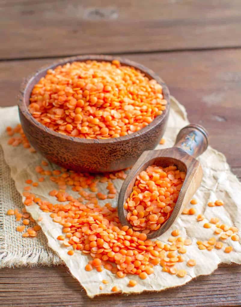 A bowl of red lentils with a scoop on a towel-lined wooden counter.