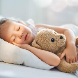 Small child sleeping in bed with her stuffed animal - a teddy bear.