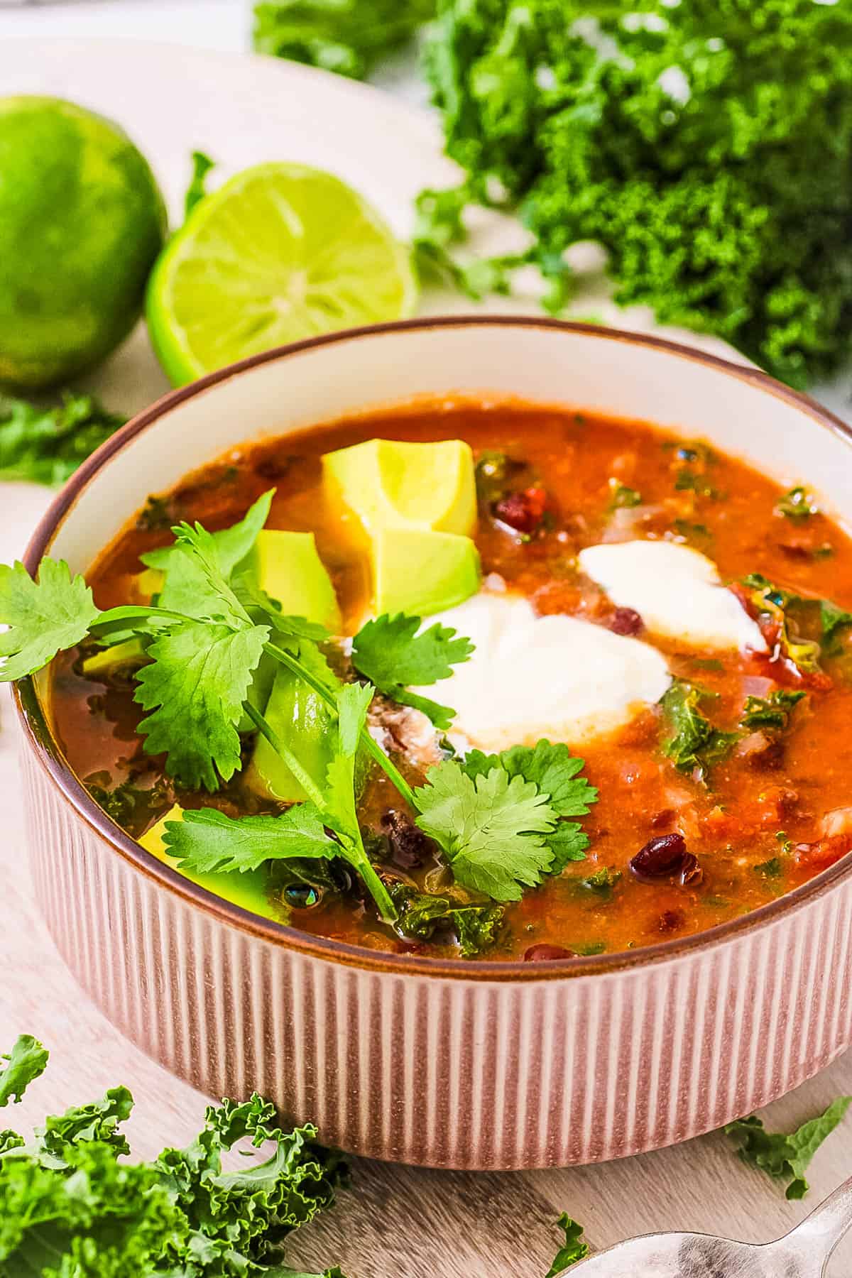 Kale and black bean soup, served in a grey bowl, garnished with avocado, cilantro, and sour cream.