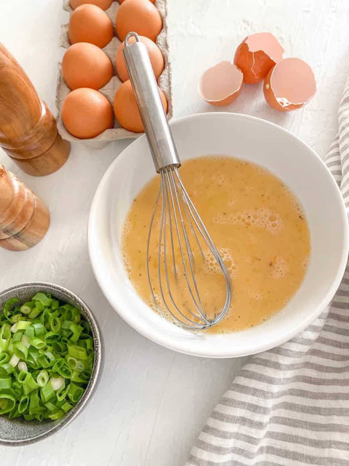 Whisking the eggs up in a white bowl on the counter with a napkin.