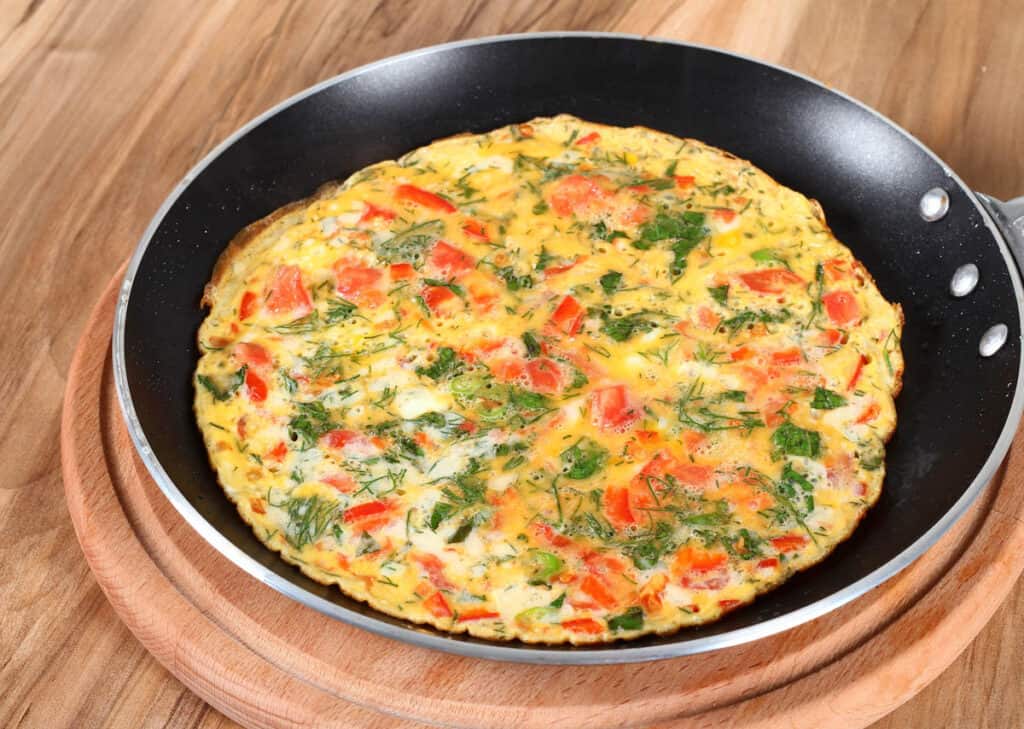 Egg white omelette with veggies in pan on wooden table.