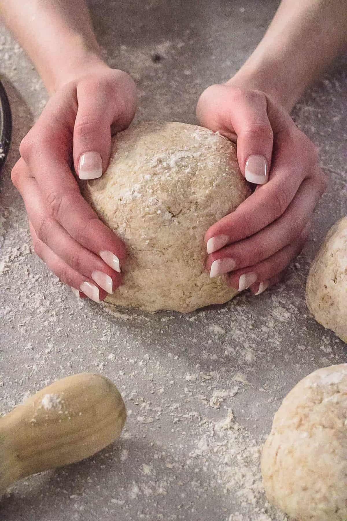 Hands ،lding a ball of low calorie pizza dough on the floured counter.