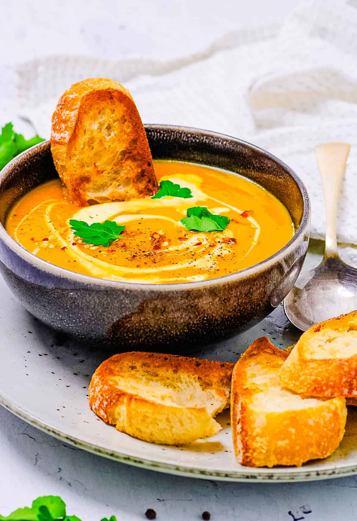 Curried sweet potato soup served in a black bowl, topped with coconut cream, crostini, and cilantro.