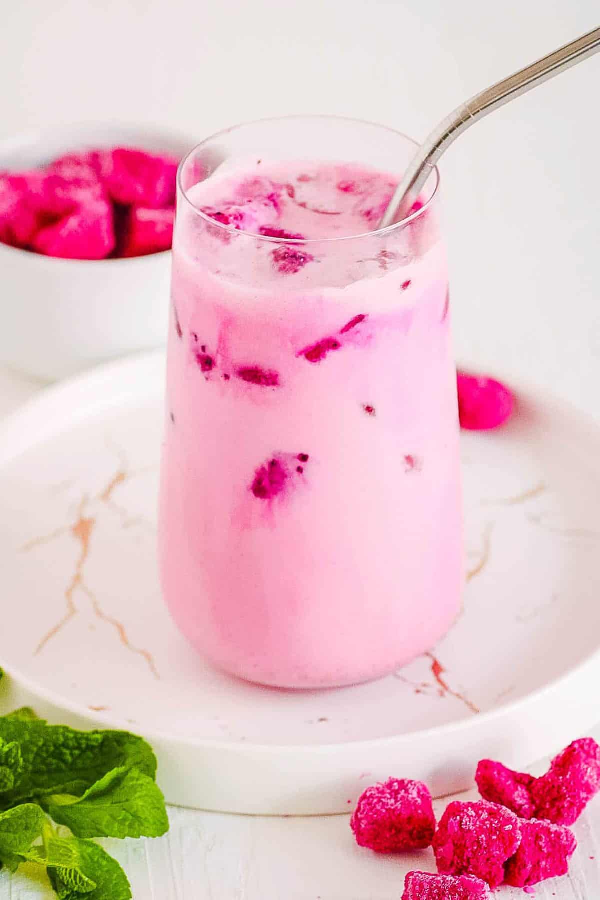 A side s،t of a gl، of Starbucks dragon fruit with a metal straw next to small cubes of dragon fruit.
