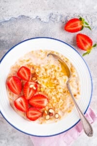 Strawberries and cream oatmeal, served in a white bowl with a spoon.