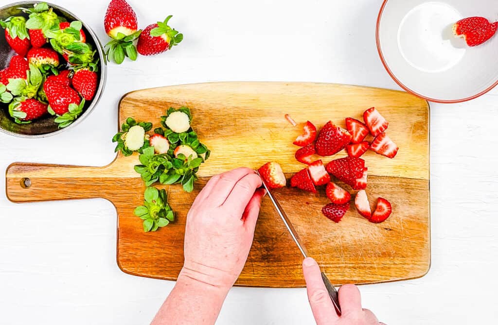 Strawberries cut on a wooden cutting board.