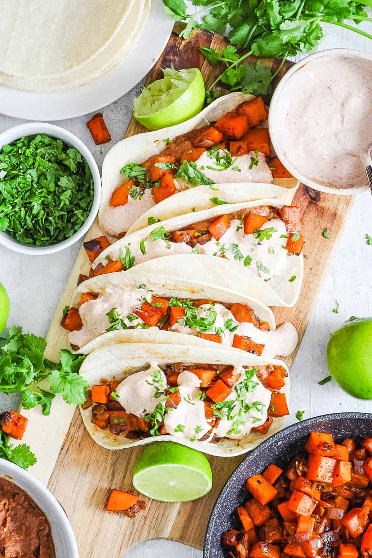 Healthy sweet potato tacos with black beans and a spicy yogurt sauce served on a wooden cutting board.