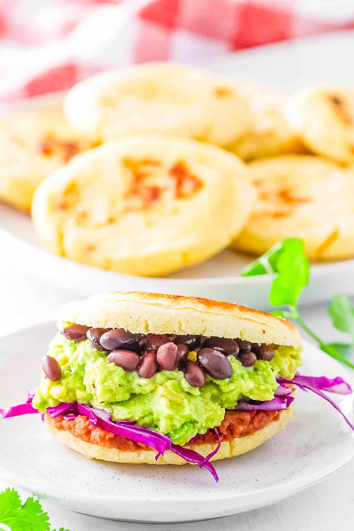 Vegan arepas stuffed with black beans, avocado and cabbage filling, served on a white plate.