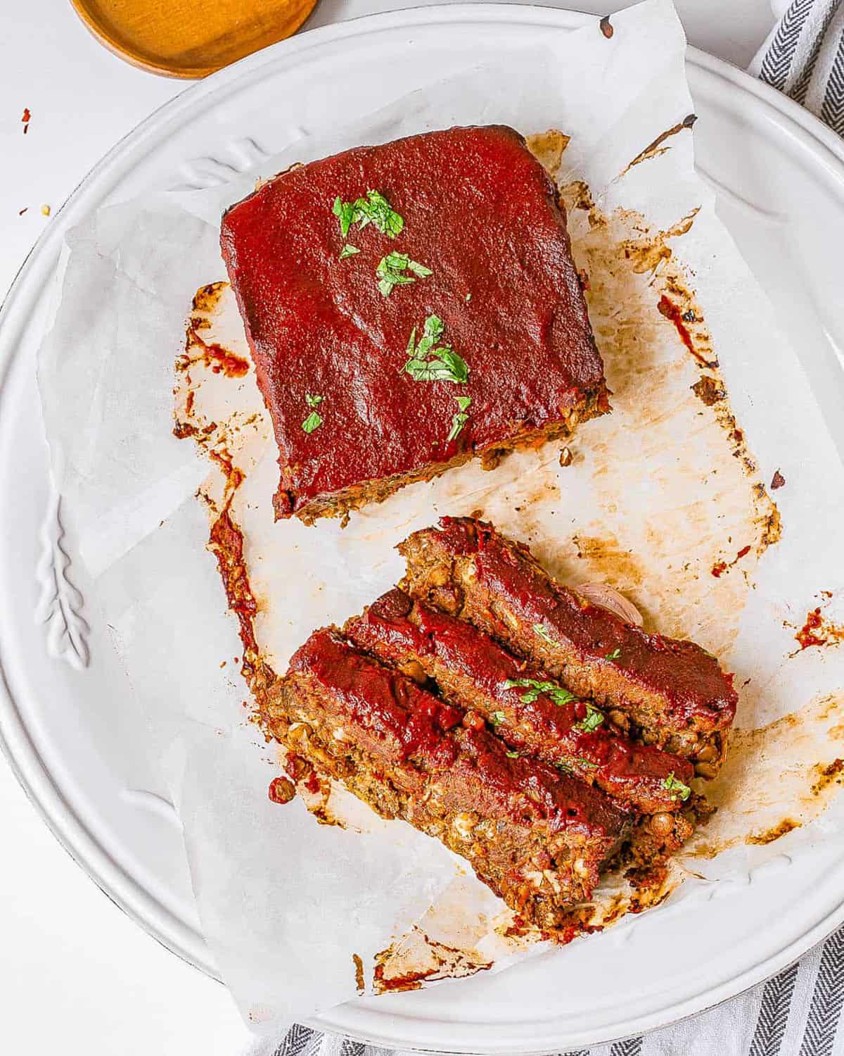 Vegan lentil loaf with tomato glaze, sliced and served on a white plate.