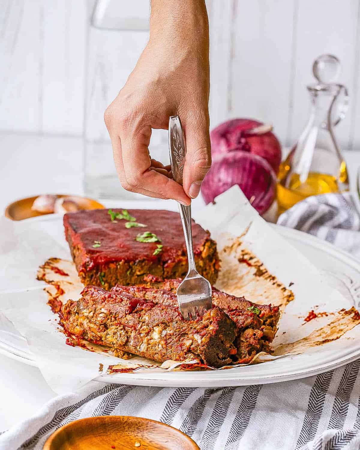 Vegan lentil meatloaf with tomato glaze, sliced and served on a white plate.