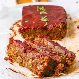Vegan meatloaf with tomato glaze, sliced and served on a white plate.