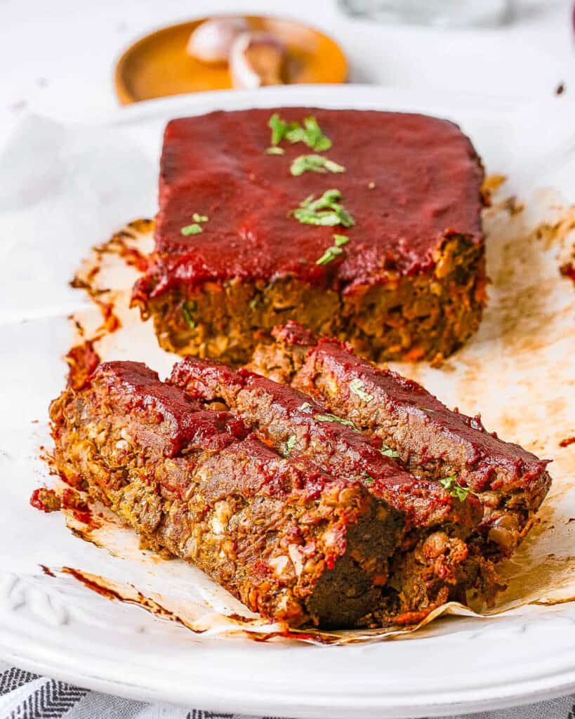 Vegan meatloaf with tomato glaze, sliced and served on a white plate.