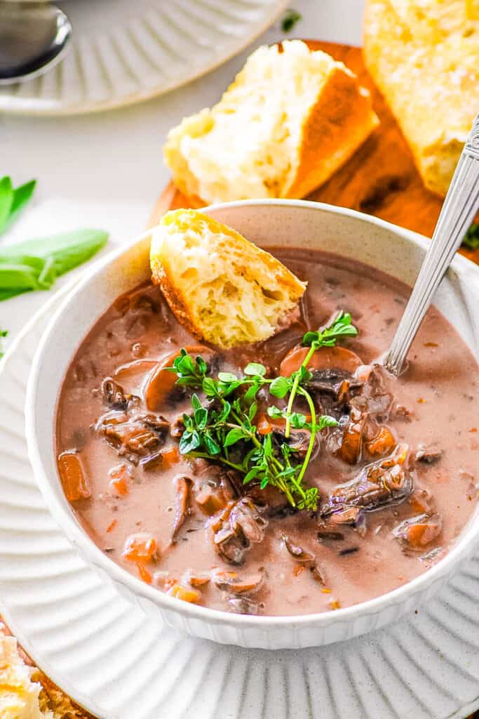 Vegan mushroom and wild rice soup, served in a white bowl, garnished with fresh herbs and a piece of crusty bread on the side.