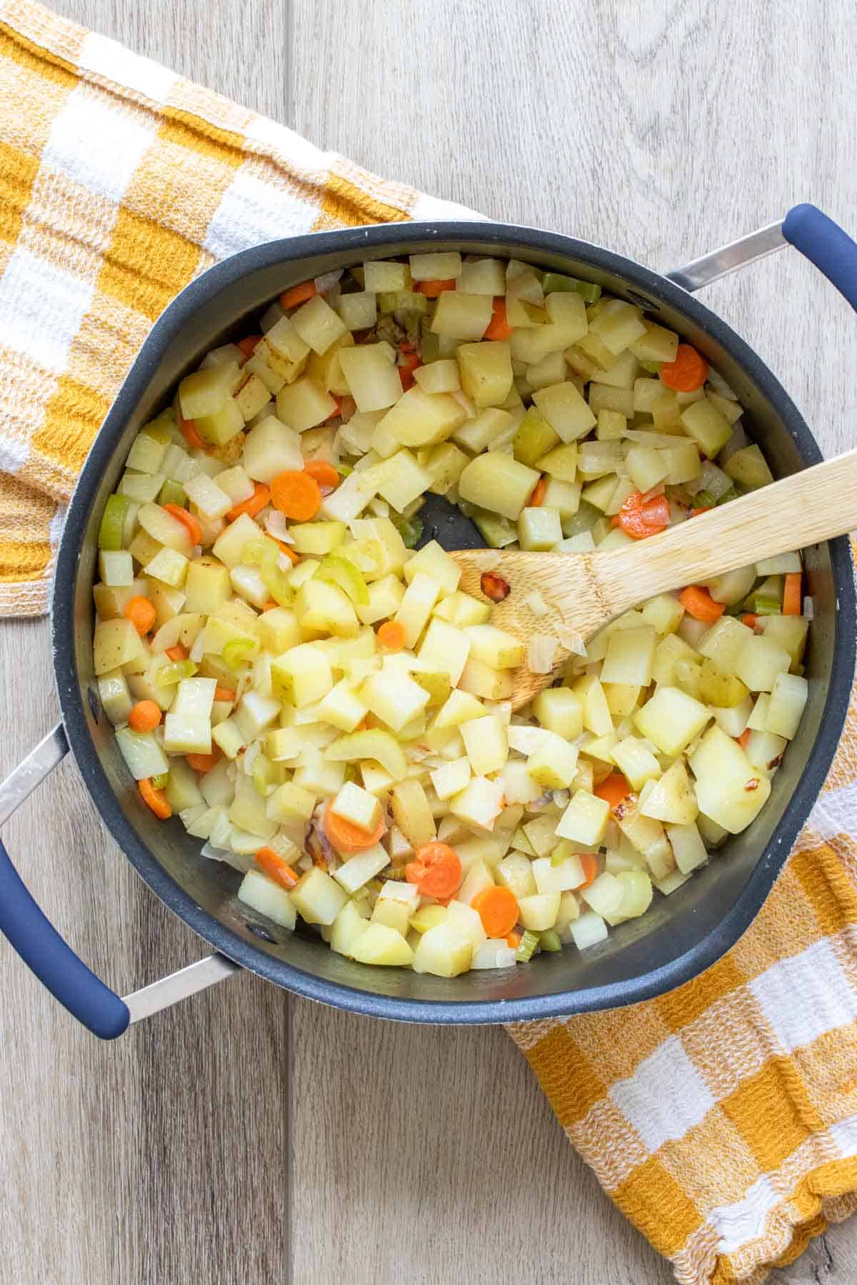 Wooden spoon mixing chopped potatoes and carrots in a black pot.