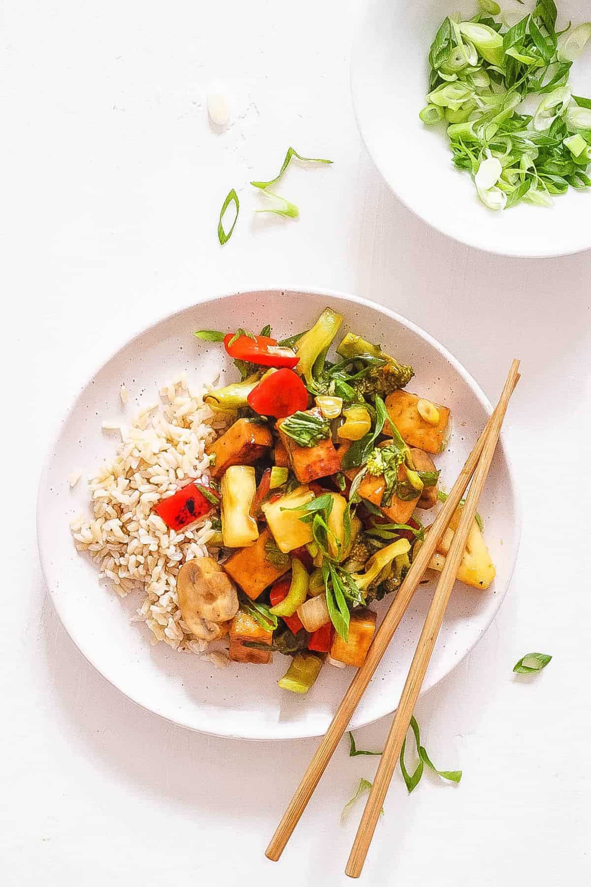 Vegan sweet and sour tofu, served on a white plate with chopsticks.