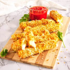 Healthy air fryer mozzarella sticks served on a wooden cutting board with tomato dipping sauce.