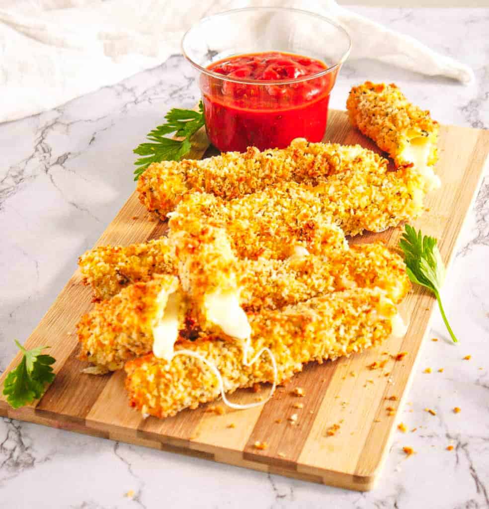 Healthy air fryer mozzarella sticks served on a wooden cutting board with tomato dipping sauce.