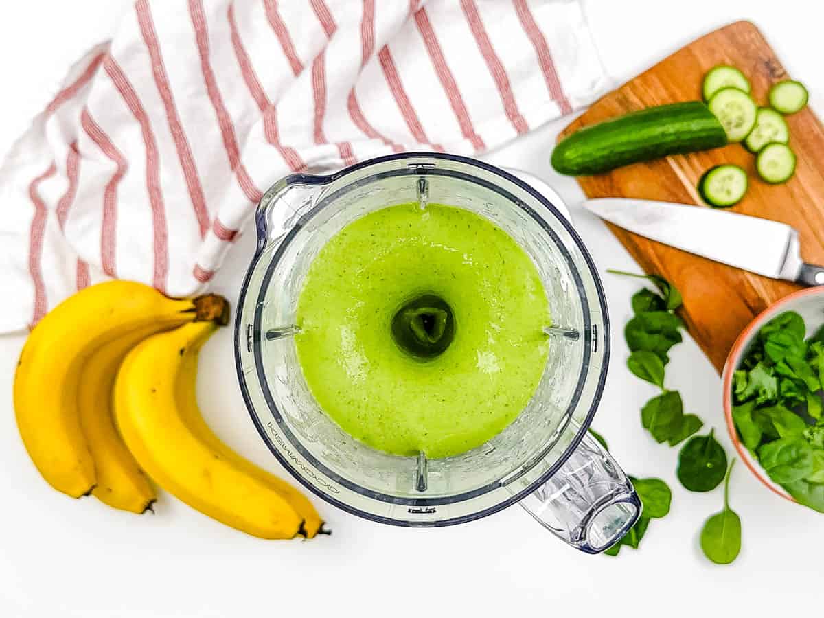 Green smoothie with pineapple and cucumber being blended in a blender.