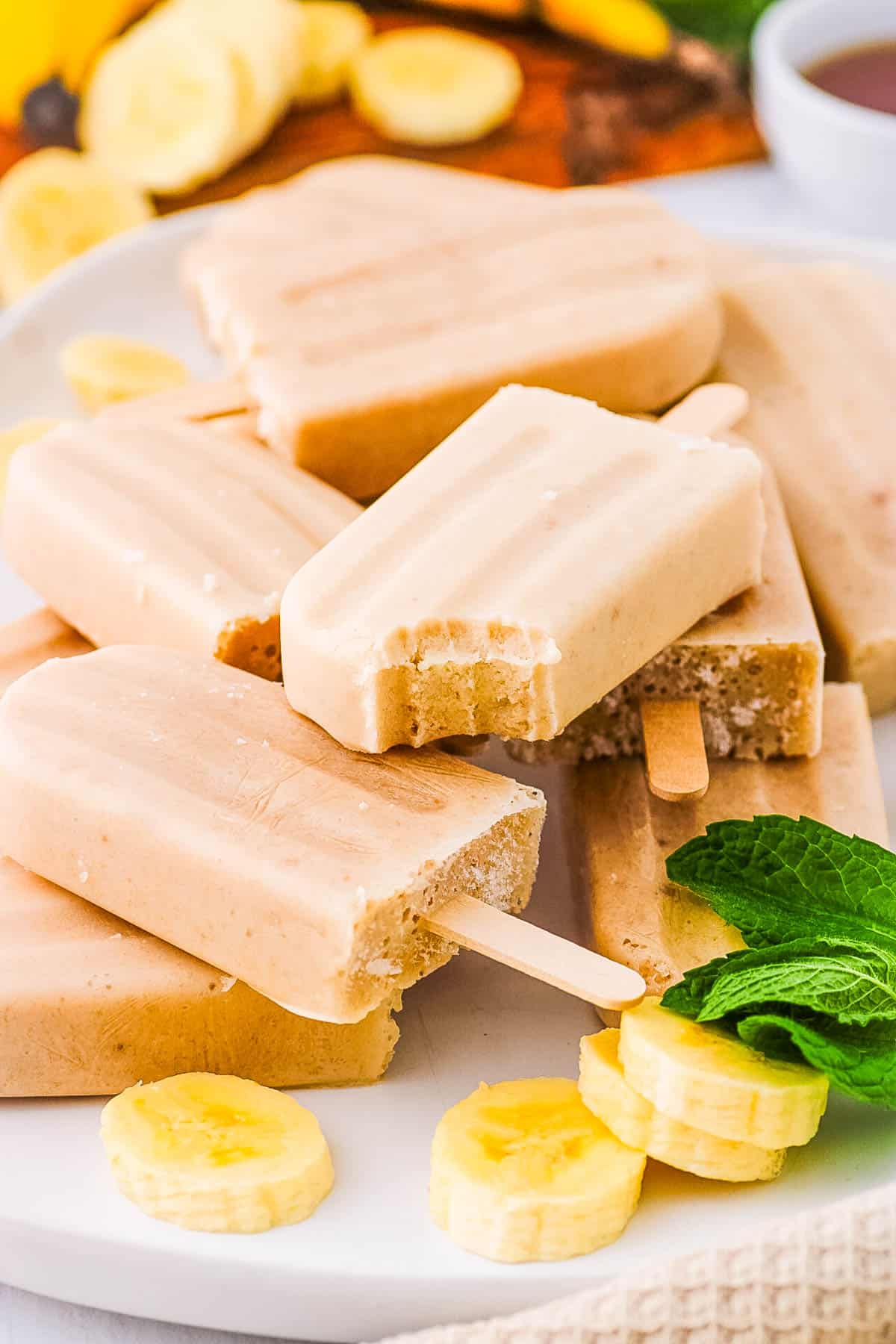 Banana popsicles served on a white tray with a bite taken out of one popsicle.