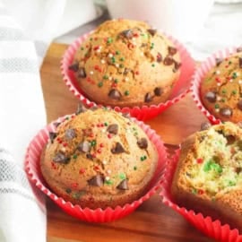 Christmas muffins with chocolate chips on a wooden cutting board.