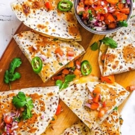 Vegan quesadillas made with butternut squash and kale topped with pico de gallo on a cutting board.