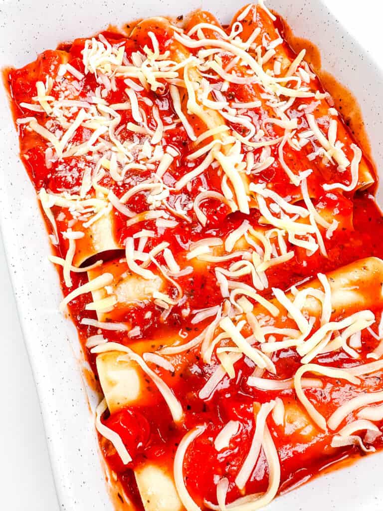 Vegetarian lasagna roll ups in a baking dish topped with marinara sauce and cheese.