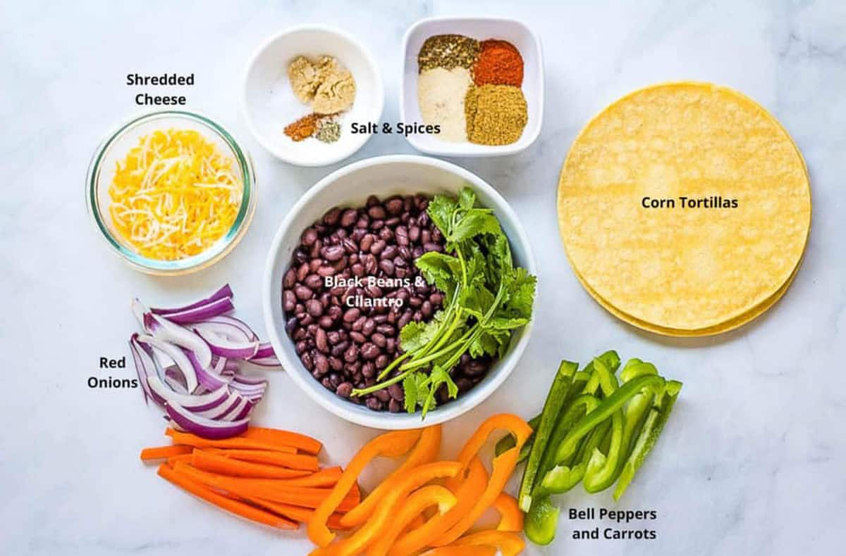 vegetarian fajita ingredients displayed in various white bowls with corn tortillas and bell peppers on the counter