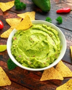 Edamame guacamole with tortilla chips in a white bowl.