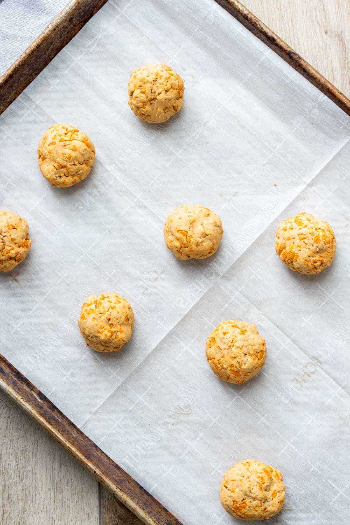 Orange colored balls on a parchment lined baking sheet.