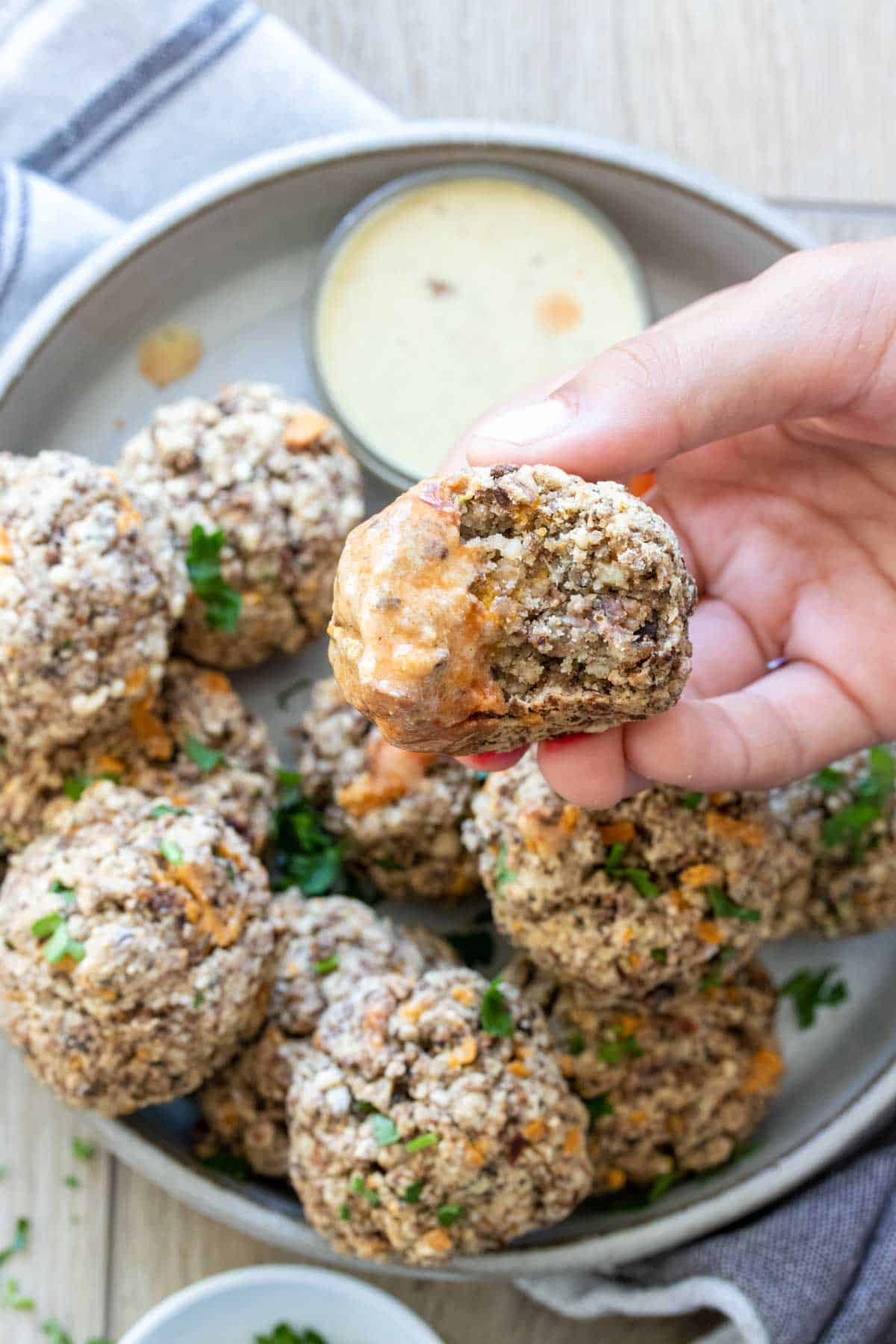 Hand holding a bitten sausage ball with an peach colored sauce on one side of it.