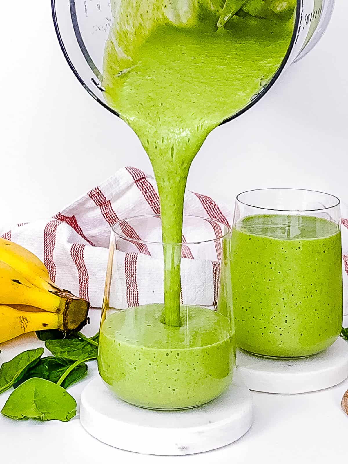 Cucumber smoothie being poured into glasses on a countertop.