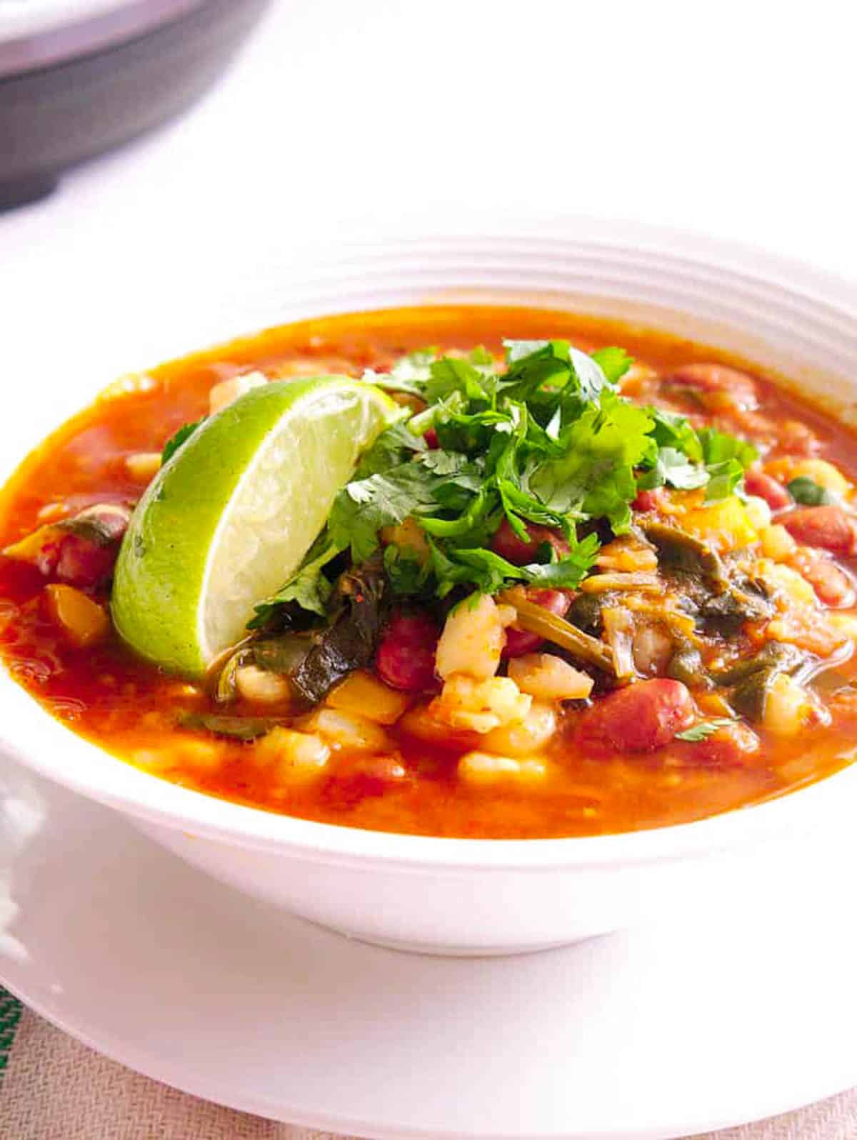Vegan pozole rojo served in a white bowl, garnished with lime and cilantro.