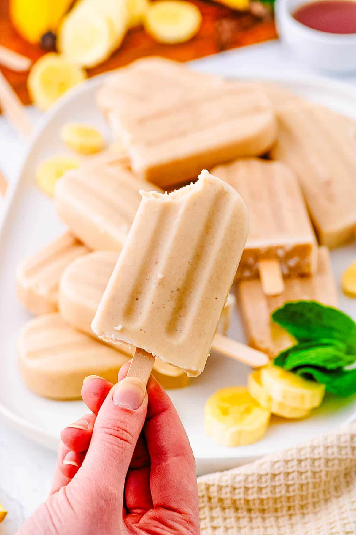 Banana popsicles served on a white tray with a hand holding up one popsicle.